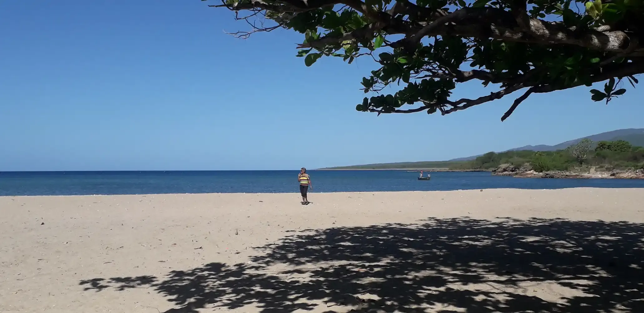 Imagen de la playa La Boca. En la arena se puede ver a una señora caminando, esa es mi abuela. En el agua hay una canoa con dos pescadores en ella.