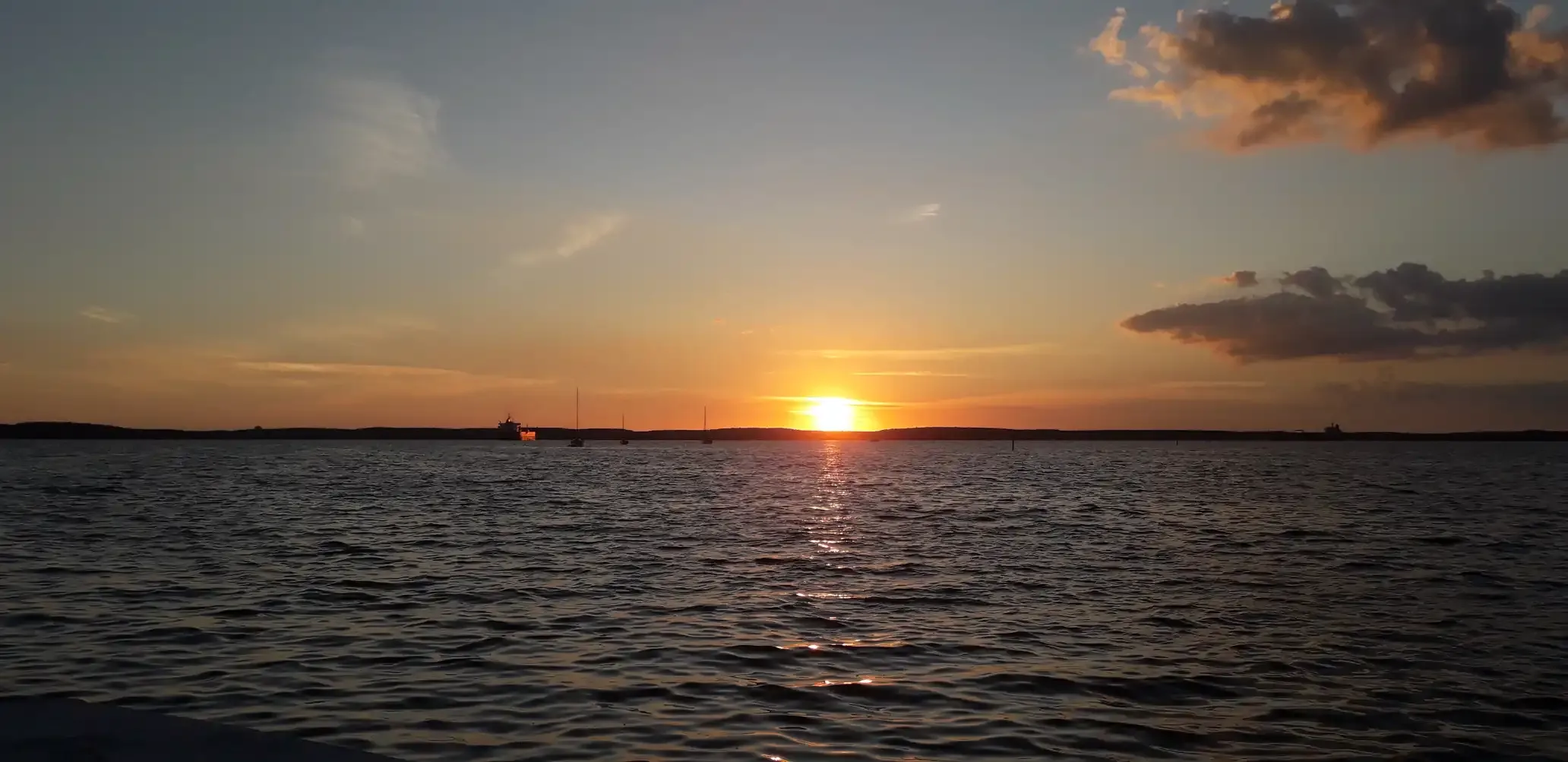 Imagen de un atardecer, el sol baja por detrás de unas lomas lejanas, después de un largo mar.